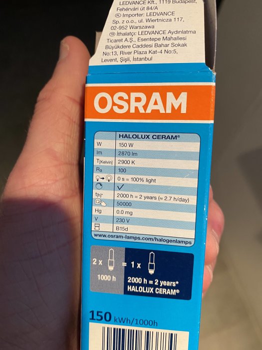 Hand håller en OSRAM HALOLUX CERAM® lampa kartong med specifikationer av 150W och 2900K.