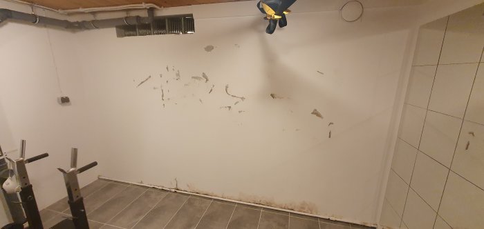 Källarvägg med flagnande färg och tecken på fuktskador och mögel.