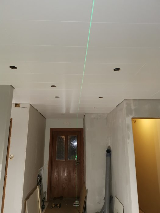 Färdigt tak i en hall med utskurna hål för belysning och en grön laserkorslinje.
