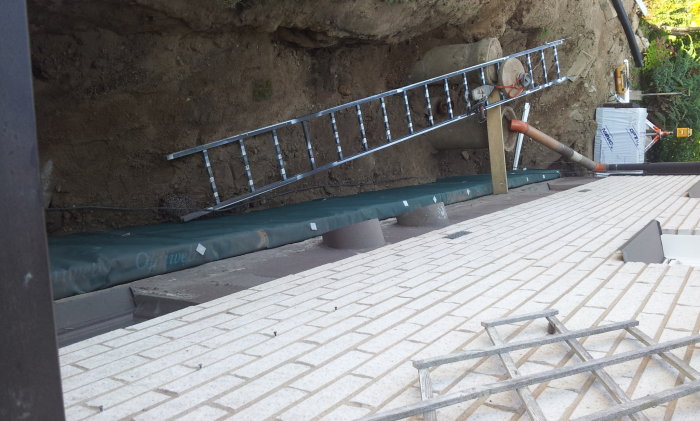 Dräneringsarbete med grus, dräneringsrör och geotextil vid husgrund på lutar tomt.