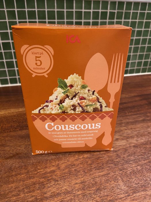 Förpackning av ICA couscous på ett träbord, med text som skämtsamt antyder att det är kossornas favoritföda.