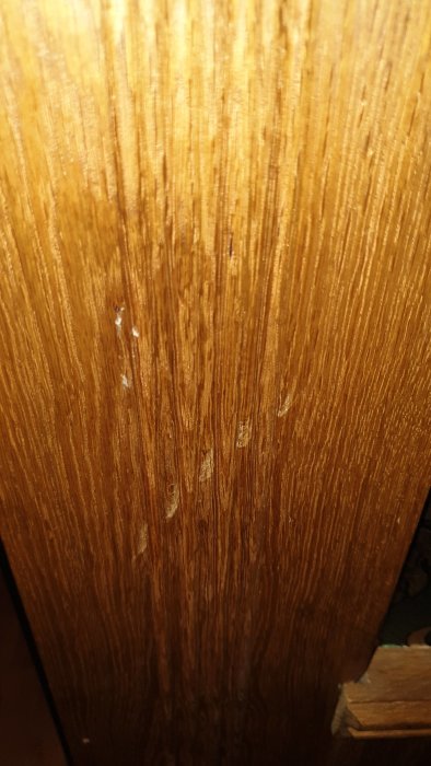 Närbild på repor och intryckta träfibrer på en mörkbrun träpanel, med något ljusare missfärgningar kring skadorna.