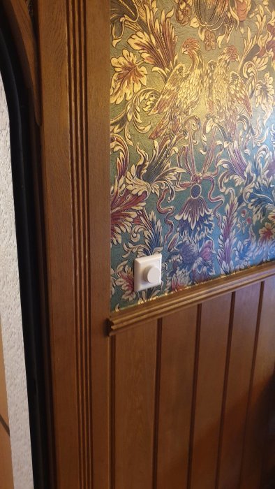 Träpaneler med repor vid dörrlist intill tapet med mönster, misstänkt skada efter städning.