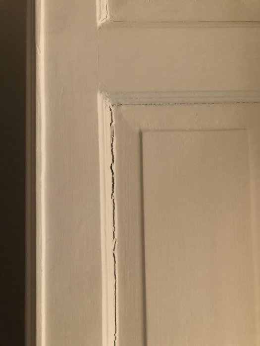 Sprickor i vita målade väggen och dörrkarmen som visar tecken på rörelse och åldrande i huset.