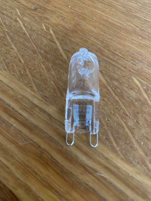 Halogenlampa med texten "18W" på träbakgrund, frågan rör dess energiförbrukning jämfört med LED.
