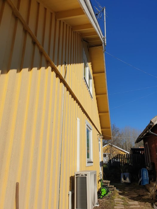 Gult hus med altan och stenlagt gångstråk, planerar att förbinda med grus och plattor.