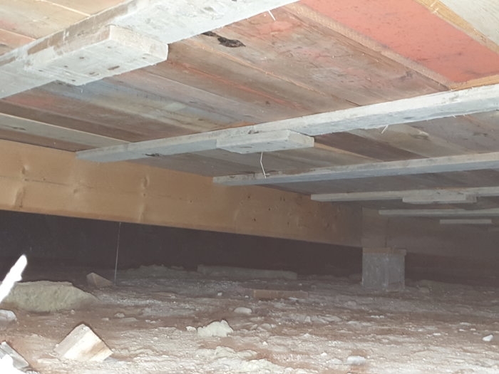 Krypgrund under hus med torr mark och ojämnt golv med böljande mönster, synliga träbjälkar och isoleringsmaterial.