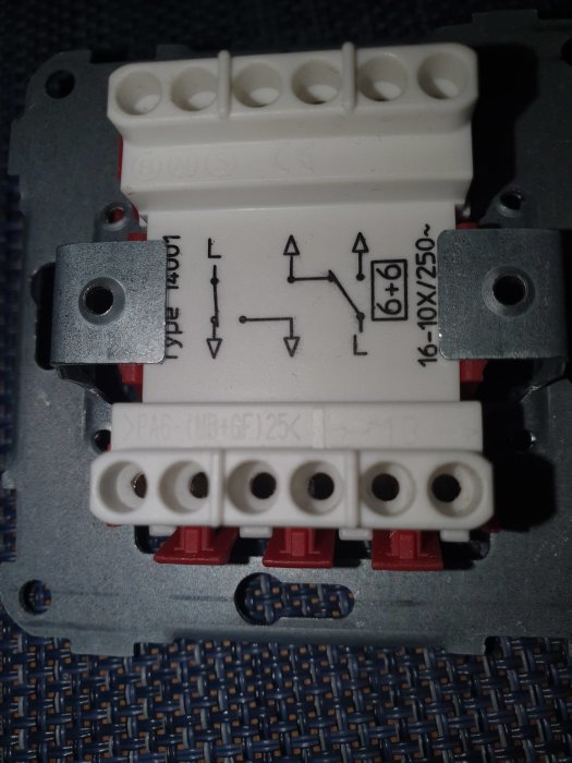 Närbild av en gammal elektrisk brytare med etiketter och kopplingshål på en vävt yta.