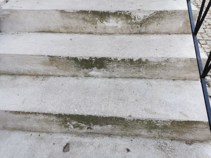 En smutsig betongtrappa med tydliga tecken på slitage och missfärgning orsakade av mögel och putssläpp.