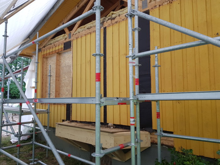 Byggnadsställningar framför hus med pågående renovering under skyddande tält.