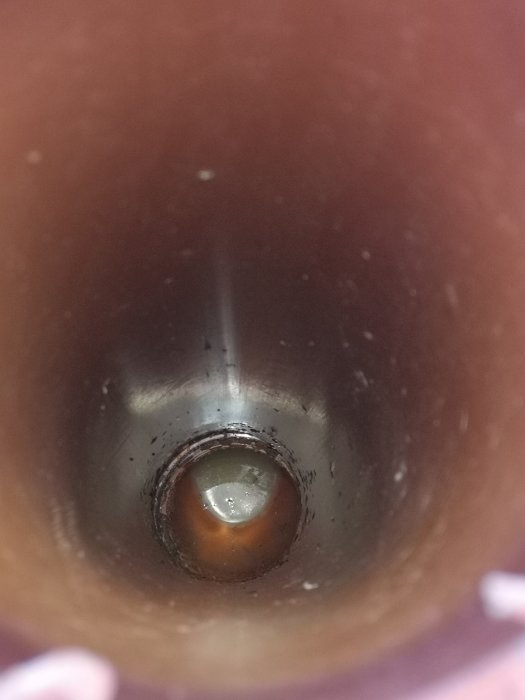 Inblick i ett mörkt avluftningsrör med stående smutsigt vatten i botten.