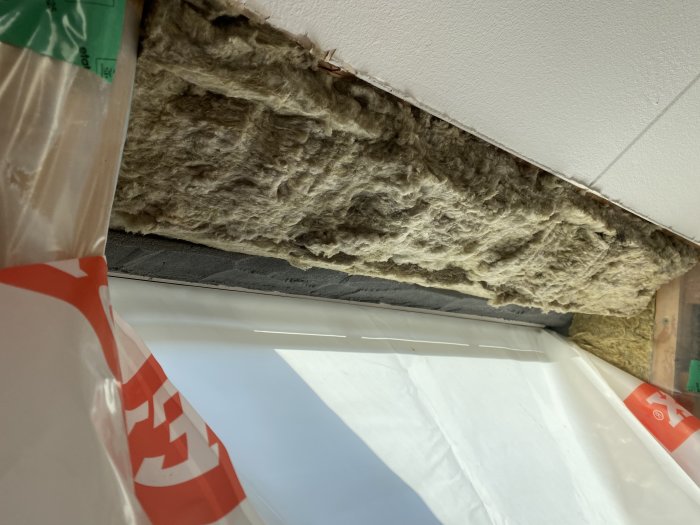 Isolering och oavslutad gipsvägg runt ett nytt takfönster med synliga spillbitar och plast.