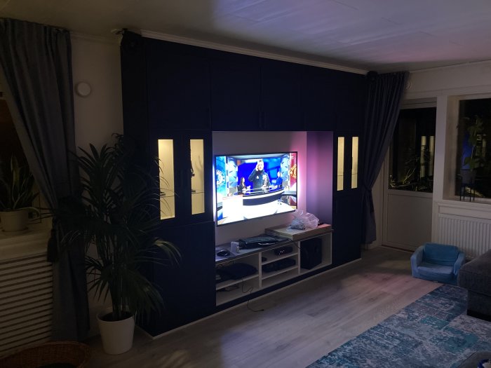 TV-hylla komplett med högtalartyg, panel och ljusramp, i ett vardagsrum med elektronik och växter.