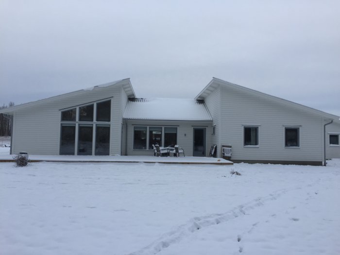 Ett nybyggt enfamiljshus med vit fasad i vinterlandskap, stora fönster och ansluten carport.