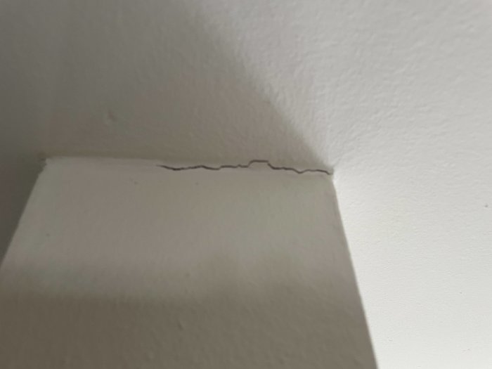 Spricka där vägg möter tak efter bredspackling som krympt över tid.