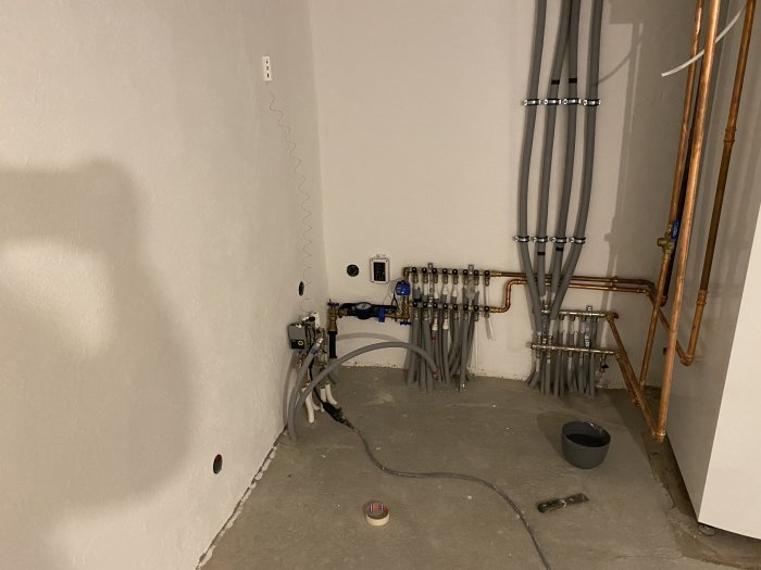 Källare med nymålade vita väggar och installerad rörsystem för vattenfördelning och elinstallationer.