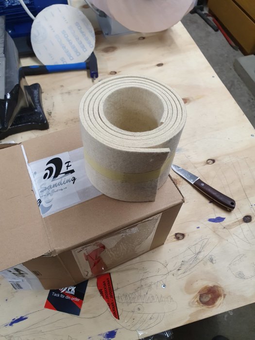 Rulle med maskinfilt på en verkstadsbänk, omgiven av en kartong och verktyg.