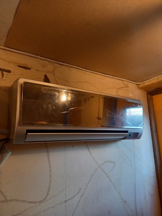 Värmepump monterad på vägg i ett renoveringsbehovande utrymme, speglar rum och tak.