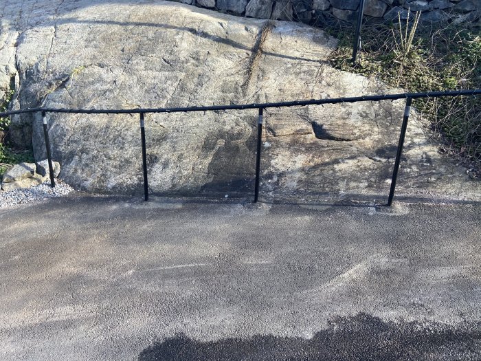 En uppfart intill ett stort berg med en svart metallräcke, där det syns tecken på vattenflöde och isbildning.