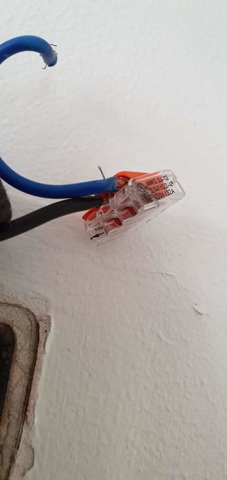 Elkabel ansluten till en klämma vid en opålitlig installation på en vit vägg.