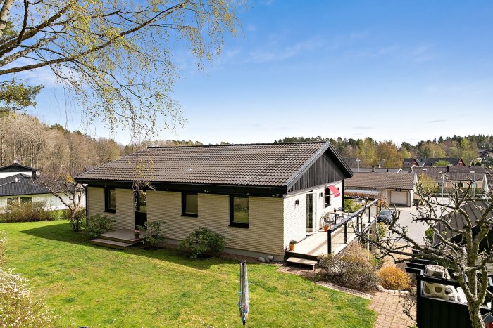 70-tals hus med vit tegelfasad, svara paneler och fönsterfoder, altandörr med svart bleck och vit dörr.