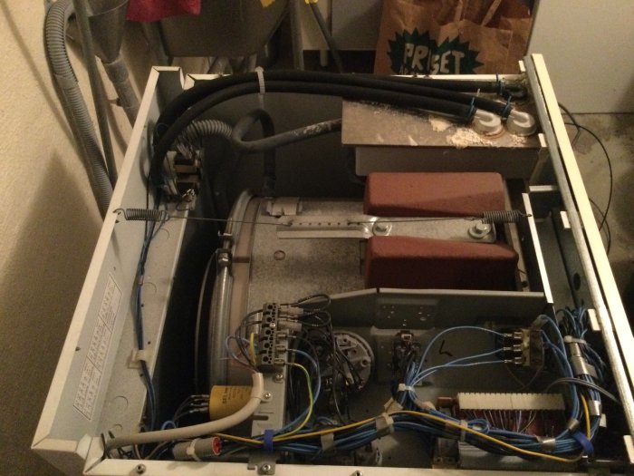 Interiör av öppen tvättmaskin visar kablar och komponenter inklusive inloppsventil och solenoider.