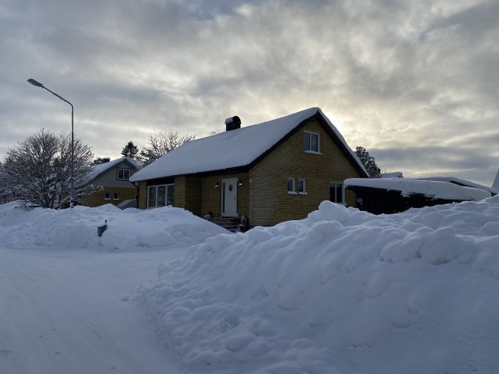 Tegelfasad småhus med snötäckt betongtak och vinterlandskap runtomkring.