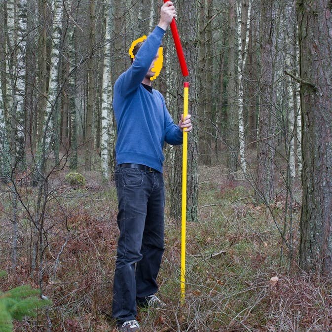 Person i skogen håller en lång gul och röd Keba-stolpe för att markera "Stenröse".