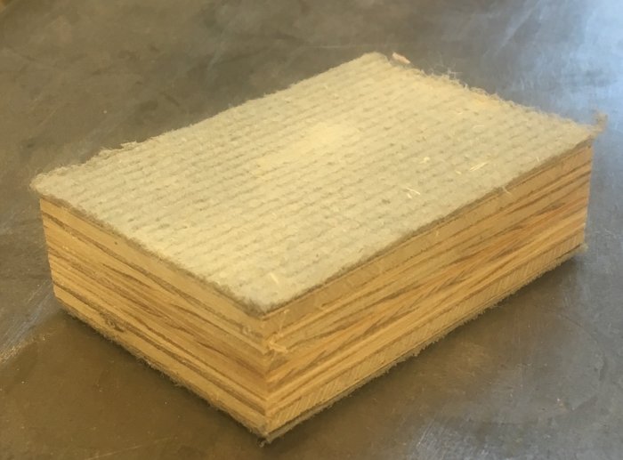 En slipkloss av plywood täckt med sandpapper på en arbetsbänk.