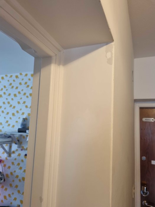 Vit dörrkarm och smyglister med synliga defekter och fläckar intill en tapetserad vägg.