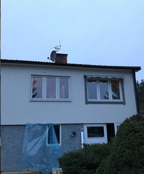 Tvåvåningshus med pågående renovering, täckt del av fasad och fönsterbyte.