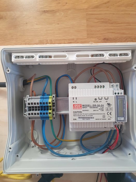 Elektrisk kapsling med nätaggregat och kabelanslutningar, installerade på vit bakgrund.
