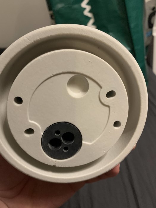 Hand håller en vit Ifö Glob-armatur med synlig rand och ofullständiga hål.