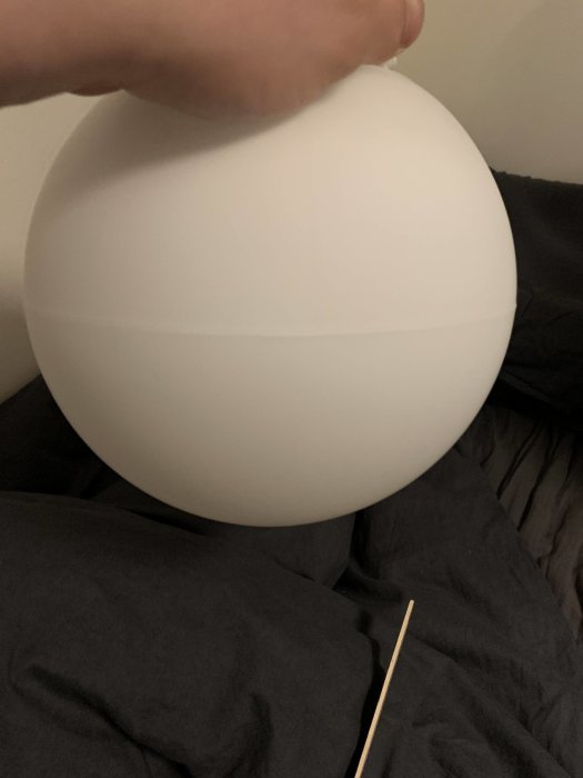 Hand som håller en Ifö Glob belysningsarmatur med synlig skarv i mitten av den opaka glasgloben, mot en mörk bakgrund.