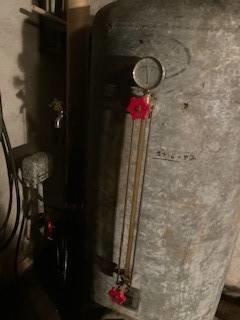 En person pekar på en tryckmätare vid 2 bar på en hydrofor i ett mörkt utrymme.