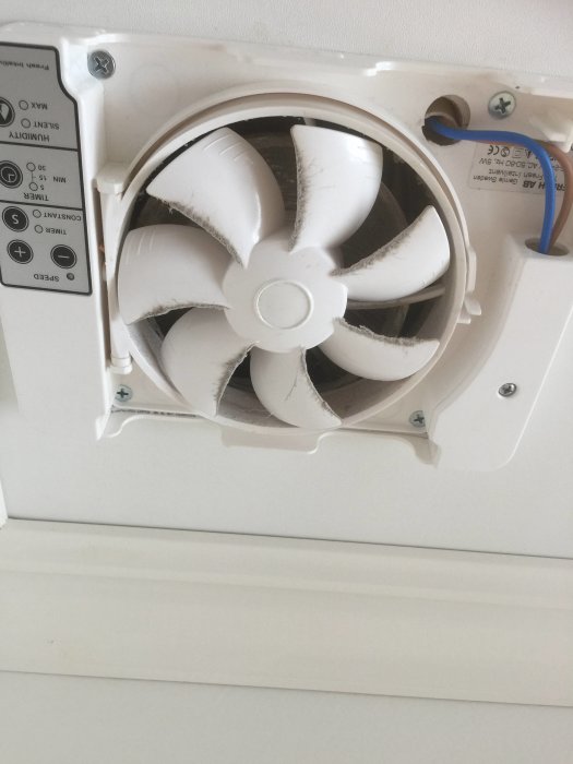 Badrumsvägg med badrumsfläkt utan stosanslutning till ventilationrör, damm på fläktbladen.
