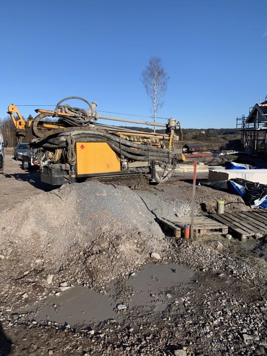 Borrutrustning för vattenbrunn på en byggarbetsplats med sten och lerpölar i förgrunden.