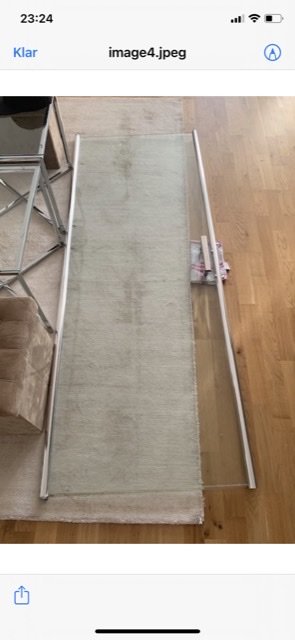 Nischduschens väggprofil placerad på ett trägolv vid en badrumsmatta, söker tillverkare för reservdel.