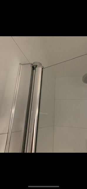 Övre delen av en nischduschdörr med synlig väggprofil och en avbruten gångled.