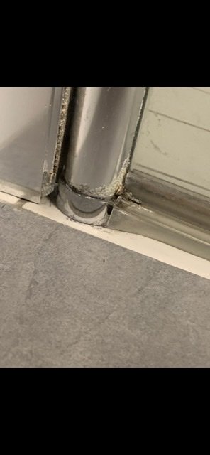 Nischduschens nedre väggprofil med skador och en avbruten gångled vid golvet.