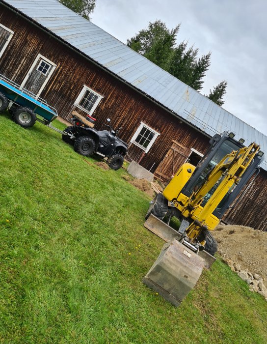 Träladugård med dubbla dörrar och gamla gångjärn, omgiven av gräsmatta, ATV och grävmaskin.