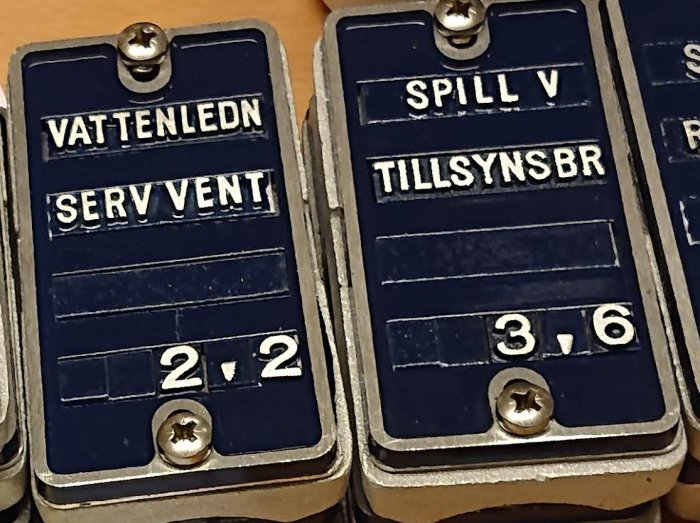 Gamla metallskyltar för VATTENLEDN SERV VENT och SPILL V TILLSYNSBR med text i vit färg.