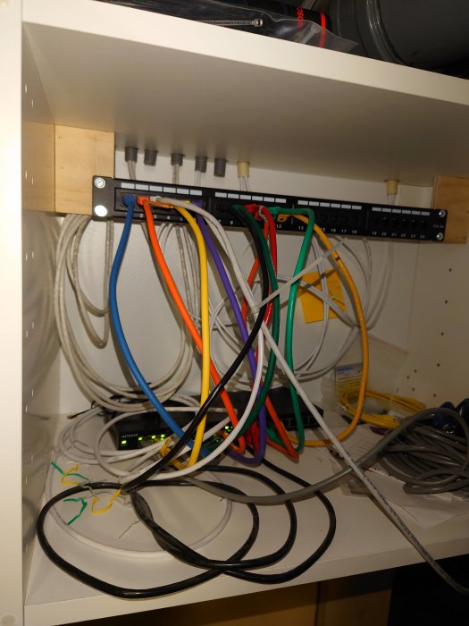 Nätverksskåp med färgglada Ethernet-kablar anslutna till patchpanel och switch.