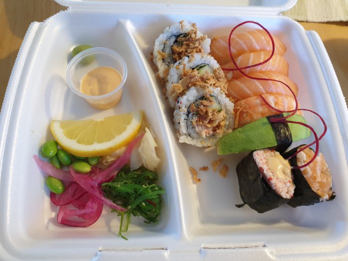 Hemkörd sushi i take-away förpackning med olika sorter inklusive nigiri och maki.