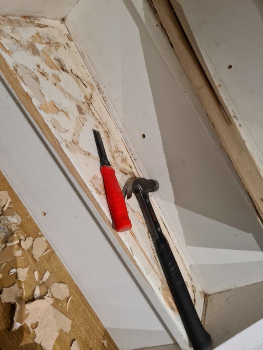 Renovering av fönsterkarm, mejsel och kofot på en vitmålad yta med avskalad färg och spill.