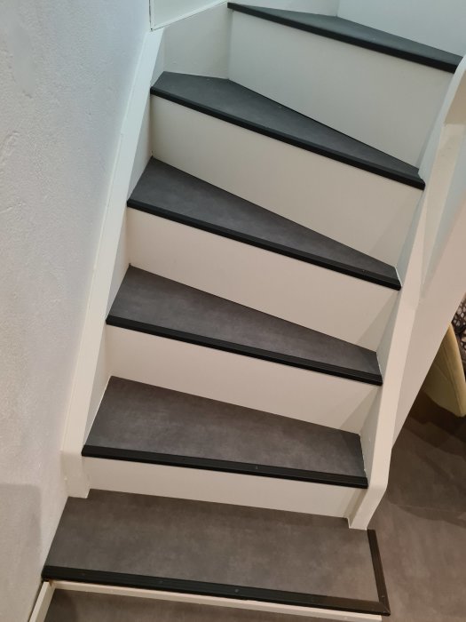 Renoverade vita trappsteg med svarta noslistar mot en vit vägg.