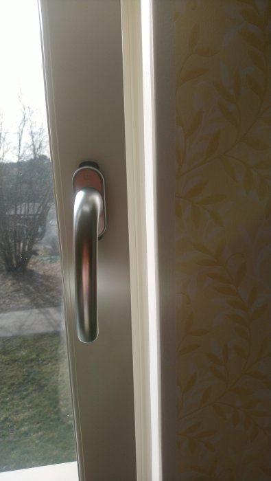 Fönstervred i stängt läge på ett nyinstallerat fönster, med vitt karm och tapet synlig i bakgrunden.