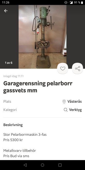 En gammal pelarborrmaskin i ett garage med borrar på hyllan under.