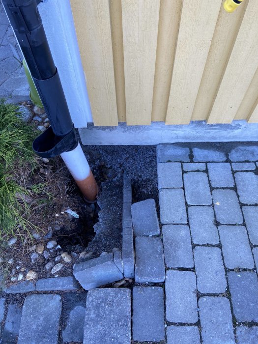 Grundhörn av hus utan markkontakt med synlig luftspalt, nedfallna plattor och ett stuprör.