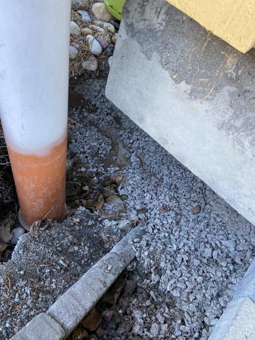 Husgrundshörn utan markkontakt, omgivet av sten och rötter med närliggande dräneringsrör.